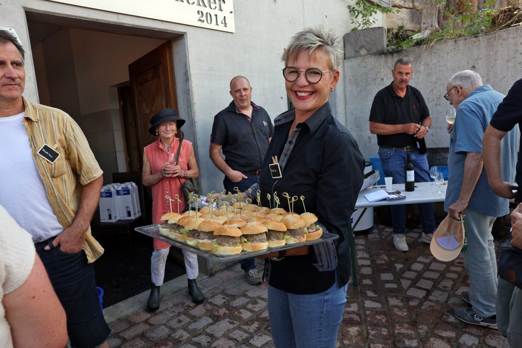 Eine strahlende Frau trägt ein Tablett voller kleiner Burger.